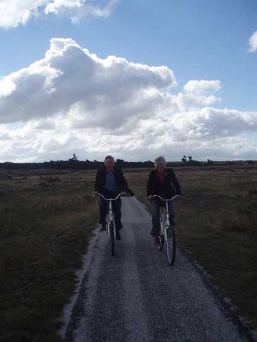 [two bicyclists sruggling against the wind, on a heath]