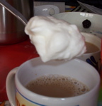 [a spoonful of whipped cream about to be added to a cup of coffee]